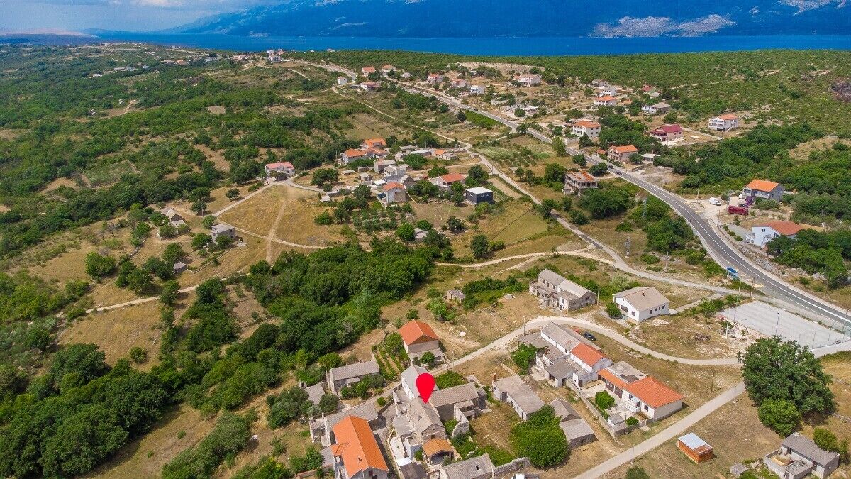 An aerial view of a coastal village with houses, roads, and a large body of water in the background.