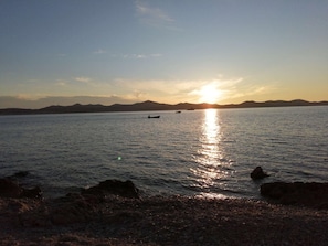 Enjoy serene views of the calm body of water and distant shoreline with a small boat anchored nearby.