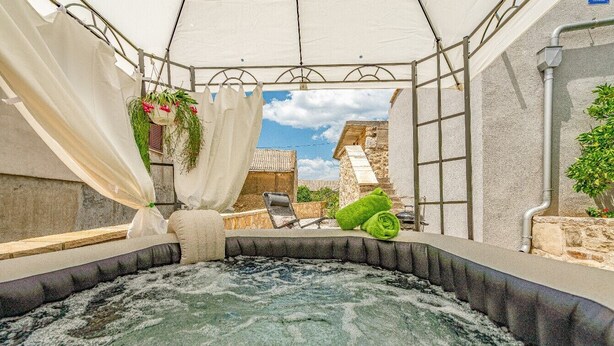 A hot tub area with a canopy, hanging plants, and a stone wall backdrop. - Holiday Home Stone Wall (Razanac)