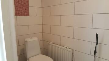 A small bathroom with white tiles, a toilet, a radiator, and a black cleaning tool leaning against the wall.