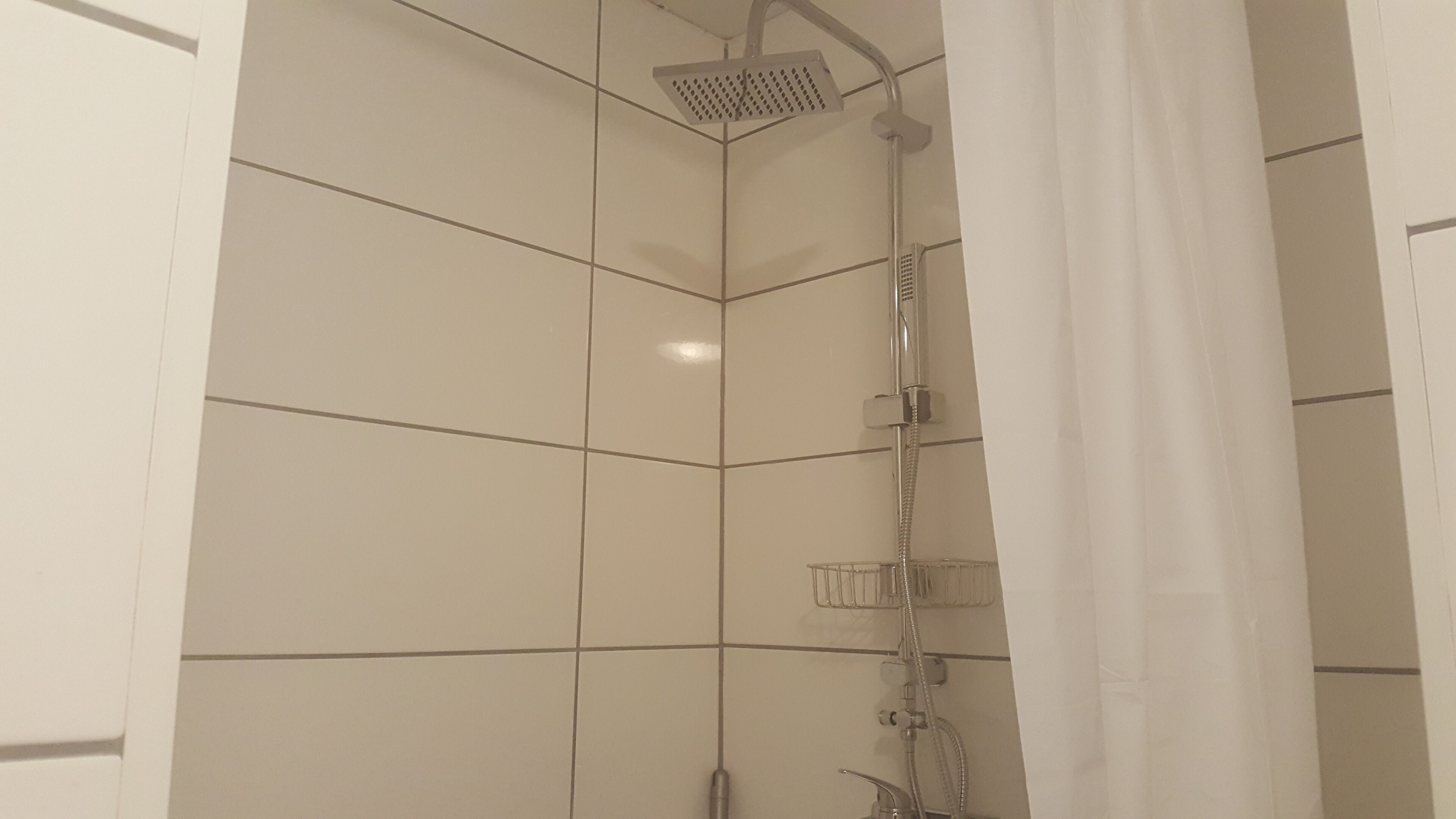 A shower with a handheld showerhead and a wall-mounted faucet.