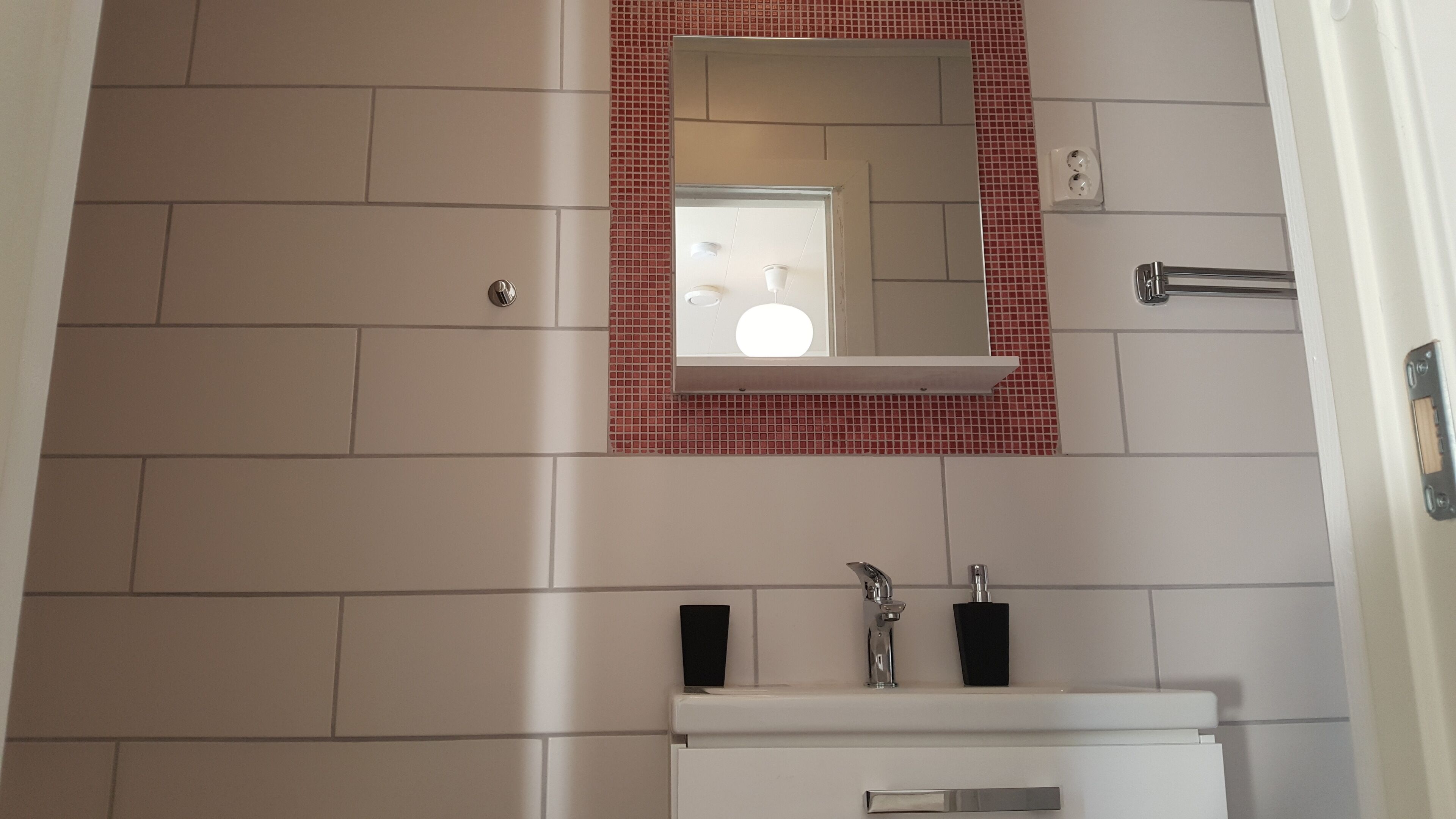 Ein Badezimmer mit einem weißen Waschbecken, einem Spiegel mit rotem Rahmen und einer gefliesten Wand.