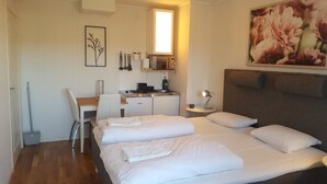 A hotel room with a bed, a desk, a chair, a small kitchenette, and a painting on the wall. - Sjötorps Hostel (Sjotorp)