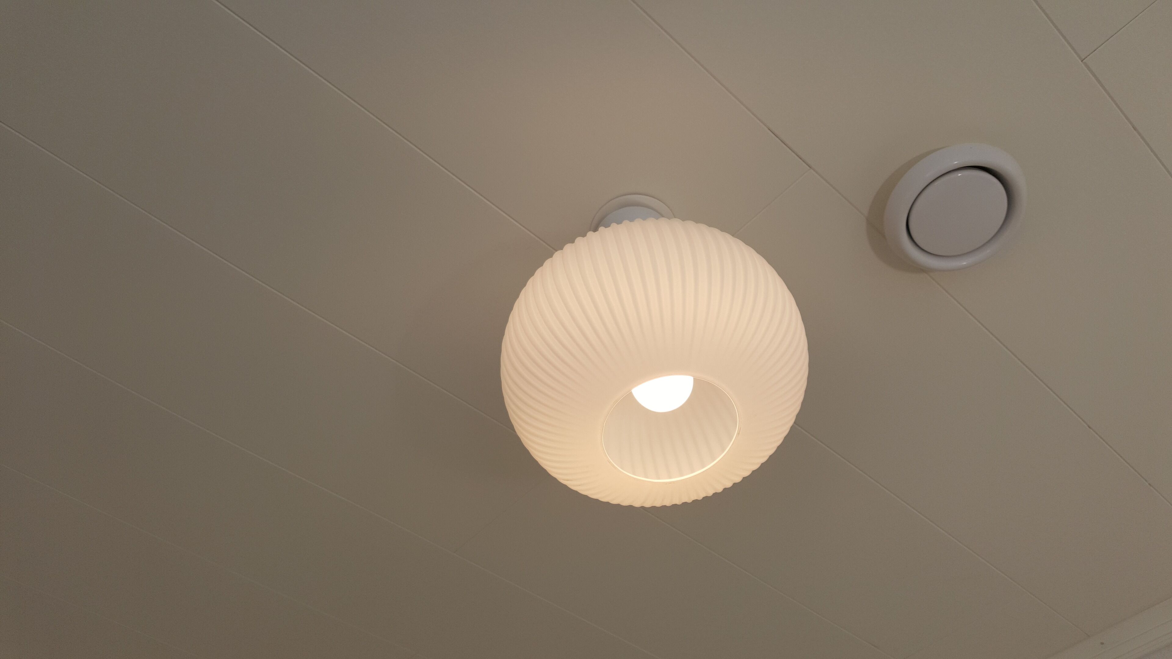 Un plafond agrémenté d’un luminaire à texture et d’un détecteur de fumée.