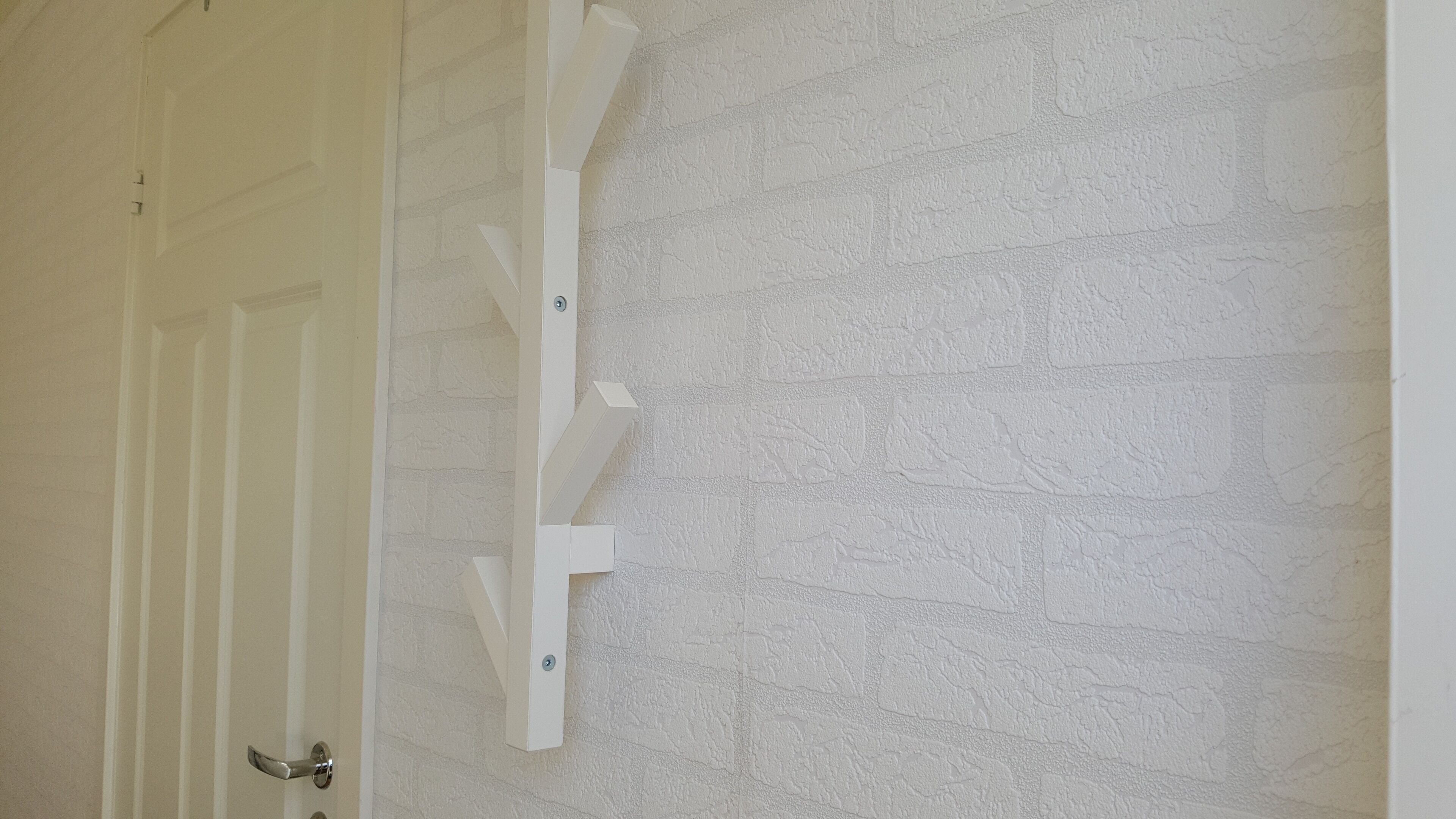 A white door with a vertical wooden shelf attached to the wall.