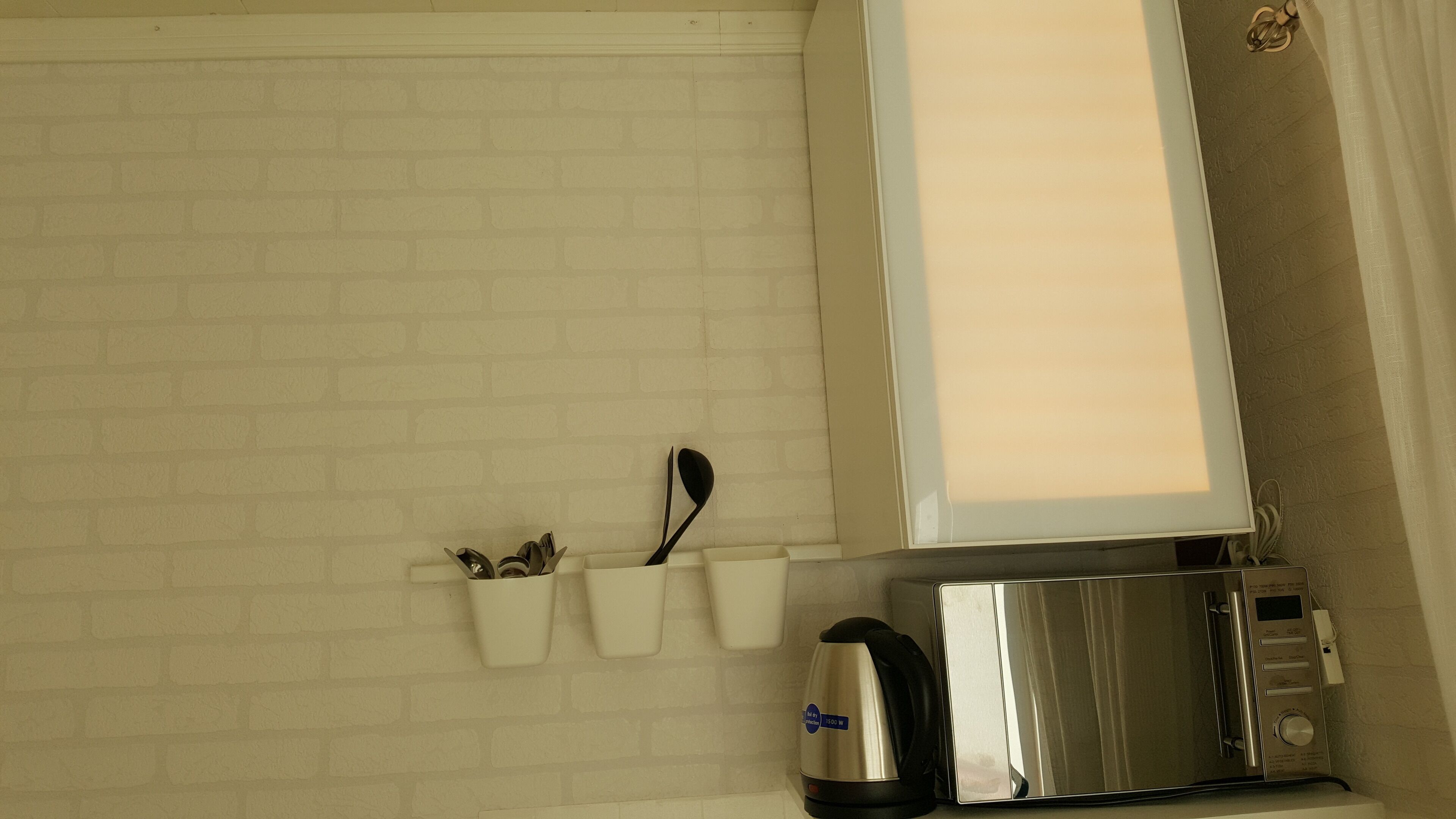 A kitchen with a white brick backsplash, a kettle, a toaster, and a window with a curtain.