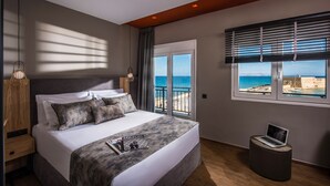 Un hotel moderno con una cama grande, un ordenador portátil sobre un reposapiés y vistas al mar a través de la ventana.