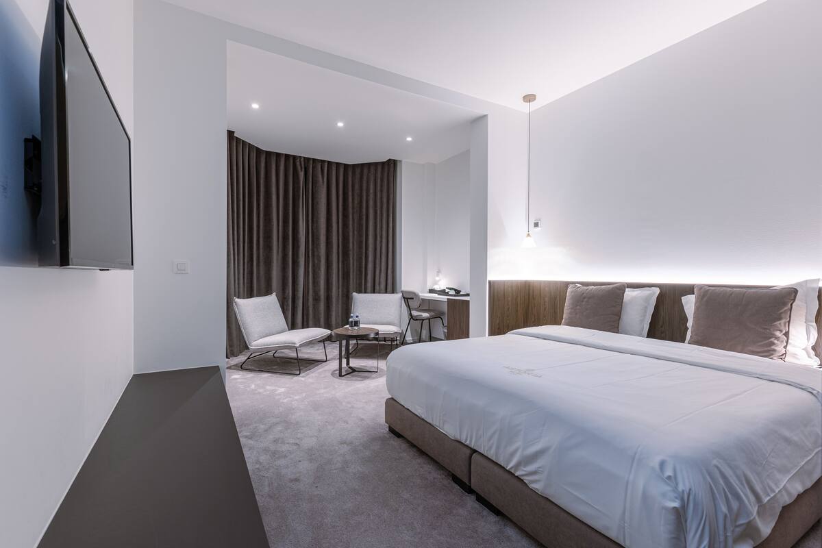 Ein modernes Hotelzimmer mit einem großen Bett, einem Schreibtisch, zwei Stühlen, einem Fernseher und einem Vorhang.