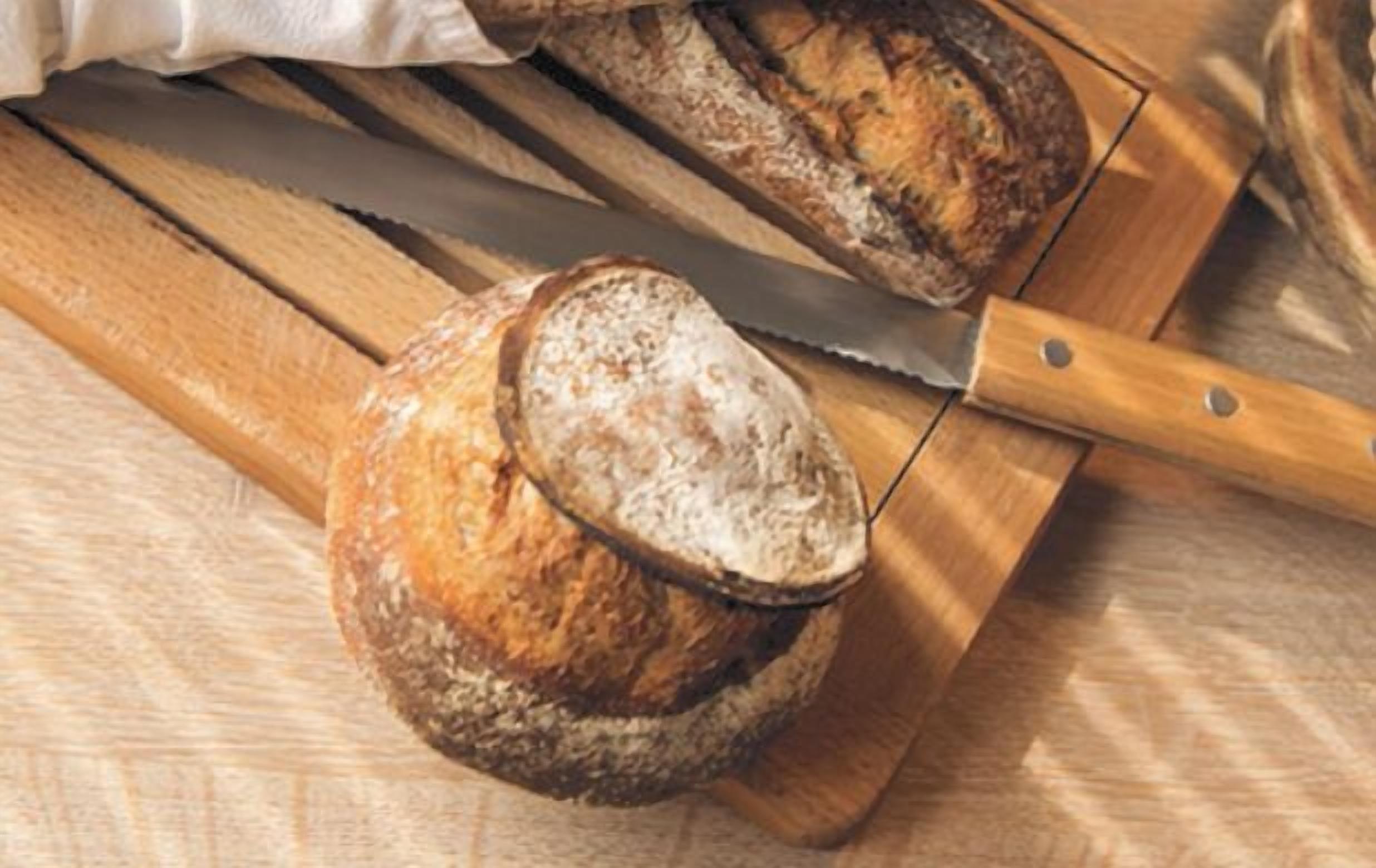 Une miche de pain sur une planche à découper en bois, avec un couteau.