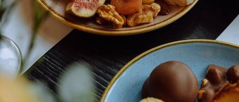 Una mesa con un plato de queso, higos y nueces, y otro plato con pasteles y un dulce cubierto de chocolate.
