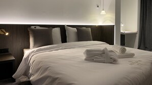 A neatly made bed with white linens and a towel, a wooden headboard, and a bedside table with a lamp. - Hotel Astoria De Haan (De Haan)