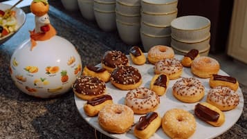 Variedad de rosquillas decoradas en un plato, con una jarra de cerámica con motivos frutales al fondo.