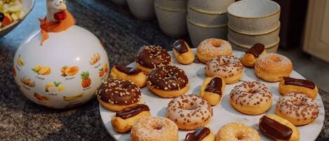 Variedad de rosquillas decoradas en un plato, con una jarra de cerámica con motivos frutales al fondo.