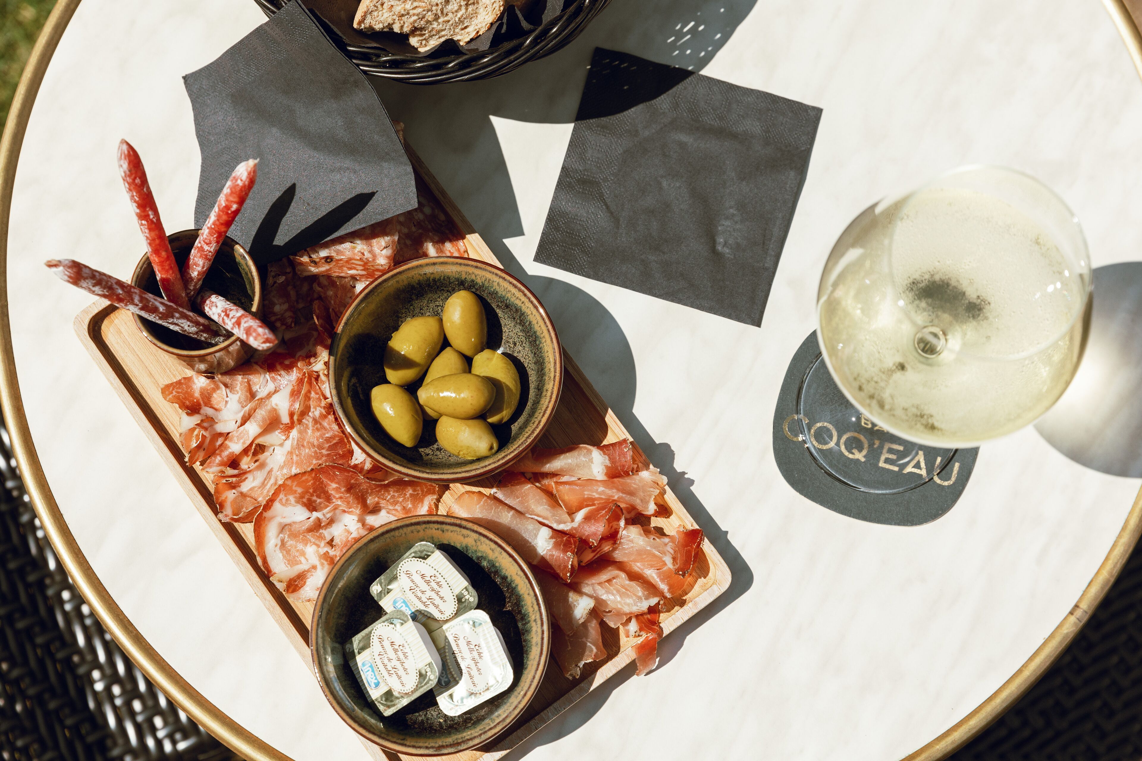 A round table with a variety of food items including cured meats, olives, and cheese, along with a glass of white wine.