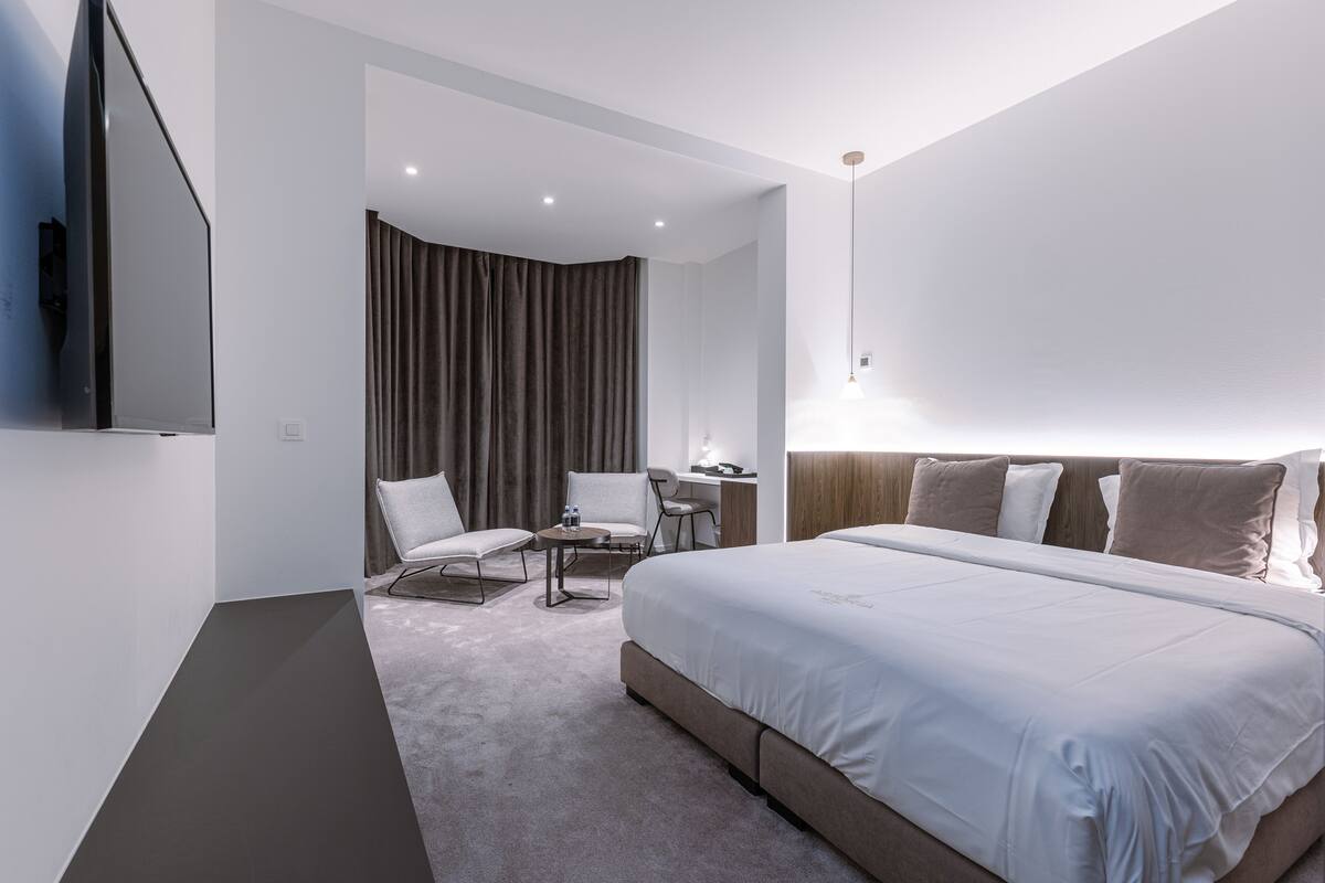 Ein modernes Hotelzimmer mit einem großen Bett, einem Schreibtisch, zwei Stühlen, einem Fernseher und einem Vorhang.