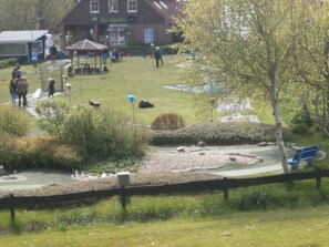 A park with a playground, picnic tables, and a building labeled "Ha'Watt." - Cozy vacation home near the beach (Dornumersiel)