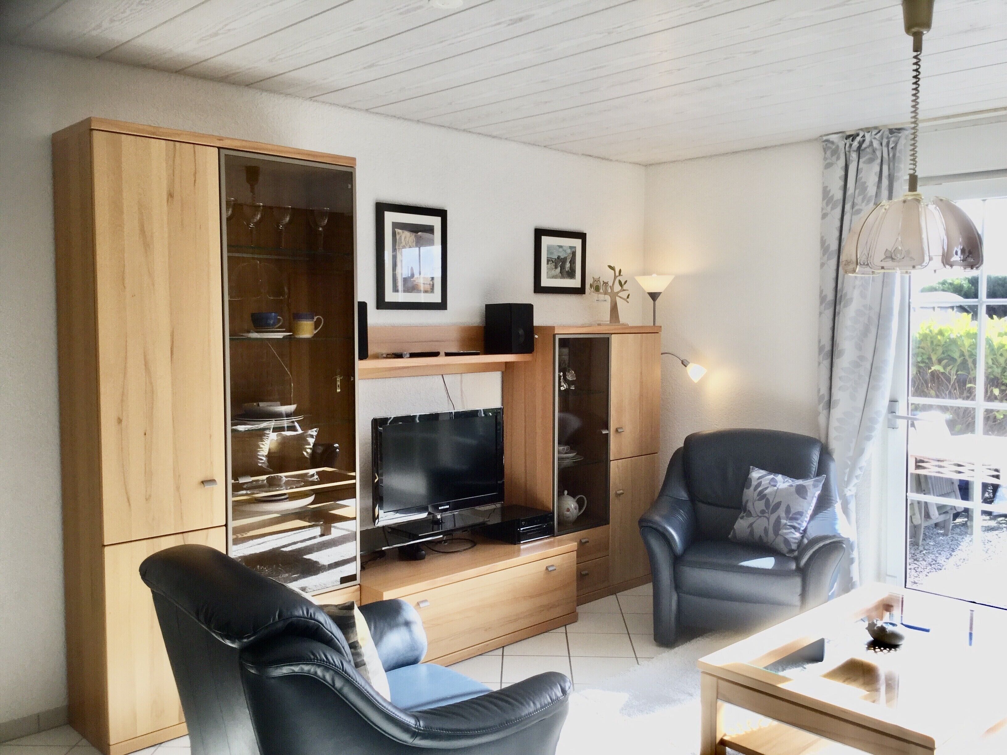 A living room with a wooden cabinet, a flat-screen TV, a black leather chair, and a table with a glass top.