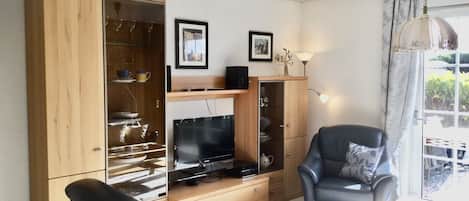 A living room with a wooden cabinet, a flat-screen TV, a black leather chair, and a table with a glass top.