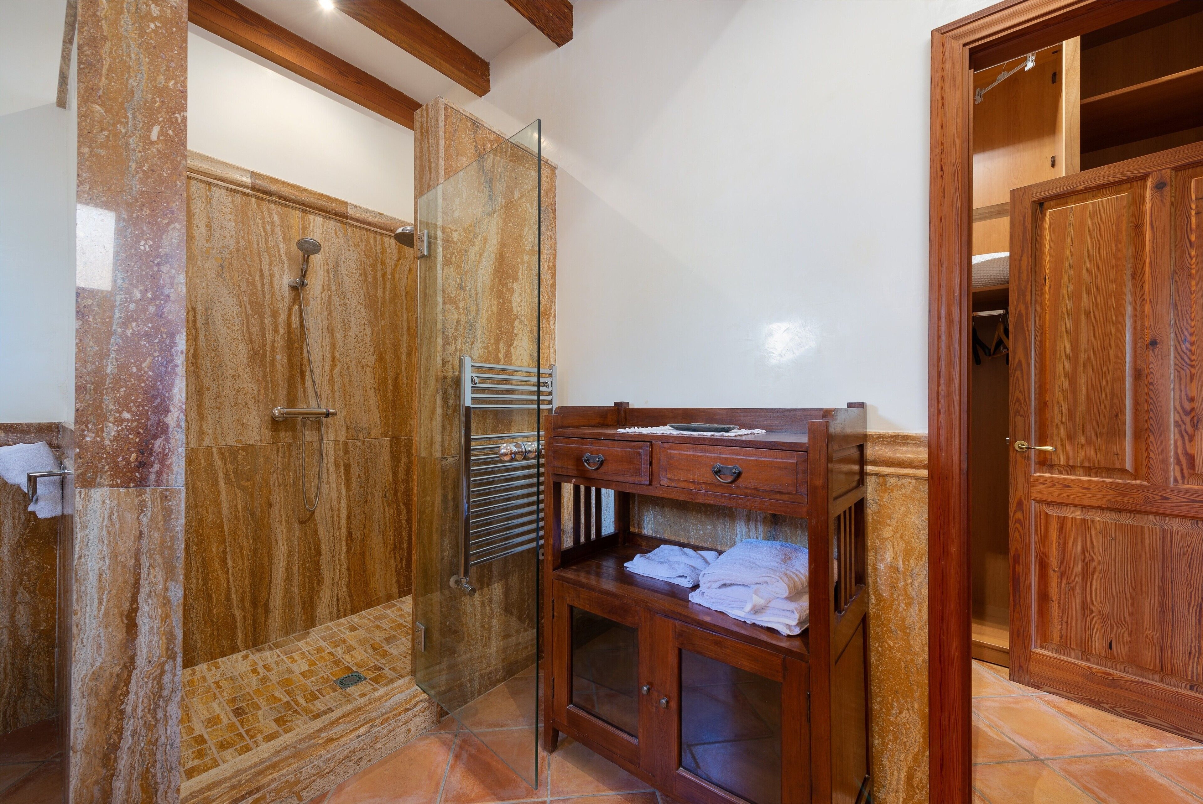 A bathroom with a glass-enclosed shower, a wooden vanity with drawers, and a tiled floor.