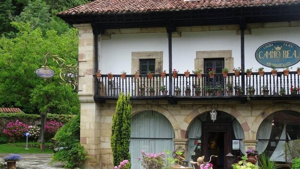 A building with a sign reading "CASA PA'CO CAMNO REA" and a balcony with potted plants. - Camino Real de Selores (Valle de Cabuerniga)