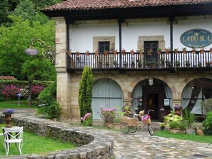 A building with a sign reading "CASA PA'CO CAMNO REA" and a balcony with potted plants. - Camino Real de Selores (Valle de Cabuerniga)