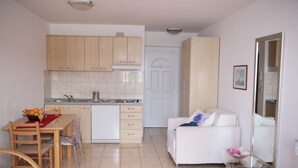A modern kitchen with wooden cabinets, a dining table with chairs, a white sofa, and a glass coffee table. - Beach Apartement - Studio Apartement - 2 Persons (Posedarje)