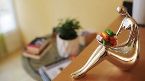 A metallic sculpture of a seated figure with a bowl of food on a wooden surface. - Beach Apartement - Studio Apartement - 2 Persons (Posedarje)