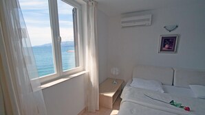 A bedroom with a bed, a bedside table, a fan, a window with curtains, and a picture on the wall. - Beach Apartement - Studio Apartement - 2 Persons (Posedarje)