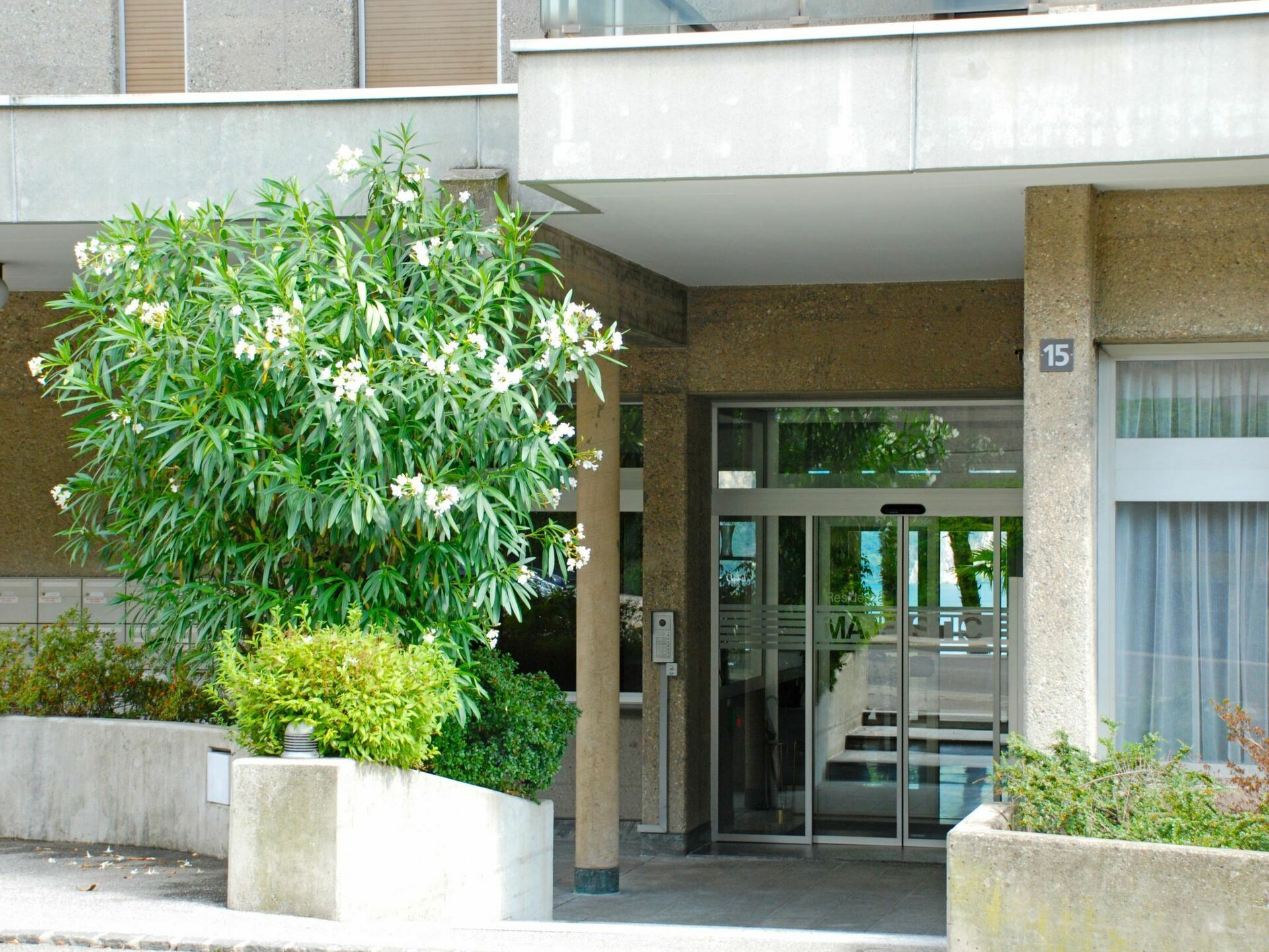 A building entrance with a glass door, a concrete planter with a tree, and a sign indicating the entrance.