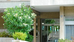 A building entrance with a glass door, a concrete planter with a tree, and a sign indicating the entrance. - Beautiful apartment for 3 guests with WIFI, TV, balcony, pets allowed and panoramic view (Sorengo)