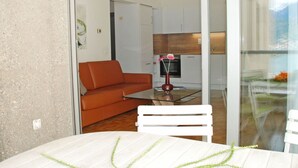 A modern living room with a glass table, a white chair, and an orange sofa. - Beautiful apartment for 3 guests with WIFI, TV, balcony, pets allowed and panoramic view (Sorengo)