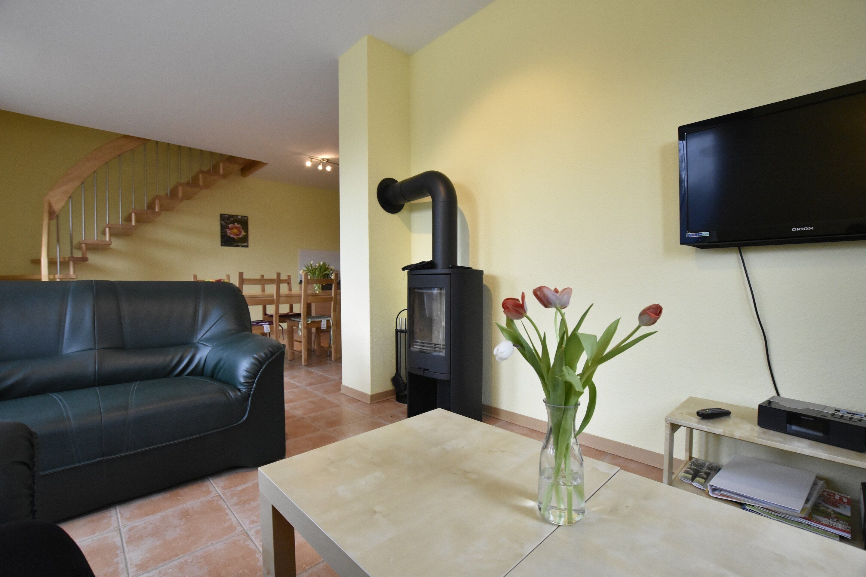 A living room with a sofa, a table with a vase, a fireplace, a TV, and a staircase.