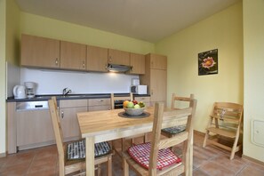 Eine Küche mit Holzausstattung, einem Esstisch mit Stühlen, einer Obstschale und einer Mikrowelle.
