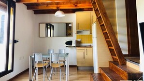Une cuisine compacte avec des poutres en bois, un coin repas avec des chaises et un escalier.