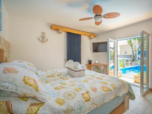 A bedroom with a bed, a ceiling fan, a TV, and a view of an outdoor swimming pool.