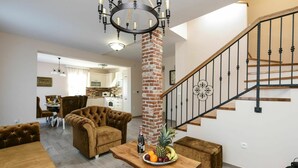 A modern living room with a brick column, a wooden dining table with fruit, and a staircase with a metal railing.