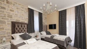 A bedroom with two beds, a stone wall, a chandelier, and a flat-screen TV.