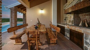 An outdoor patio with a stone fireplace, wooden benches, and a pool view.
