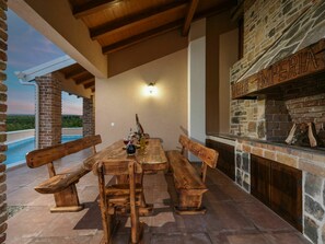 Eine Außenpatio mit Kamin aus Stein, Holzbänken und Blick auf einen Pool.