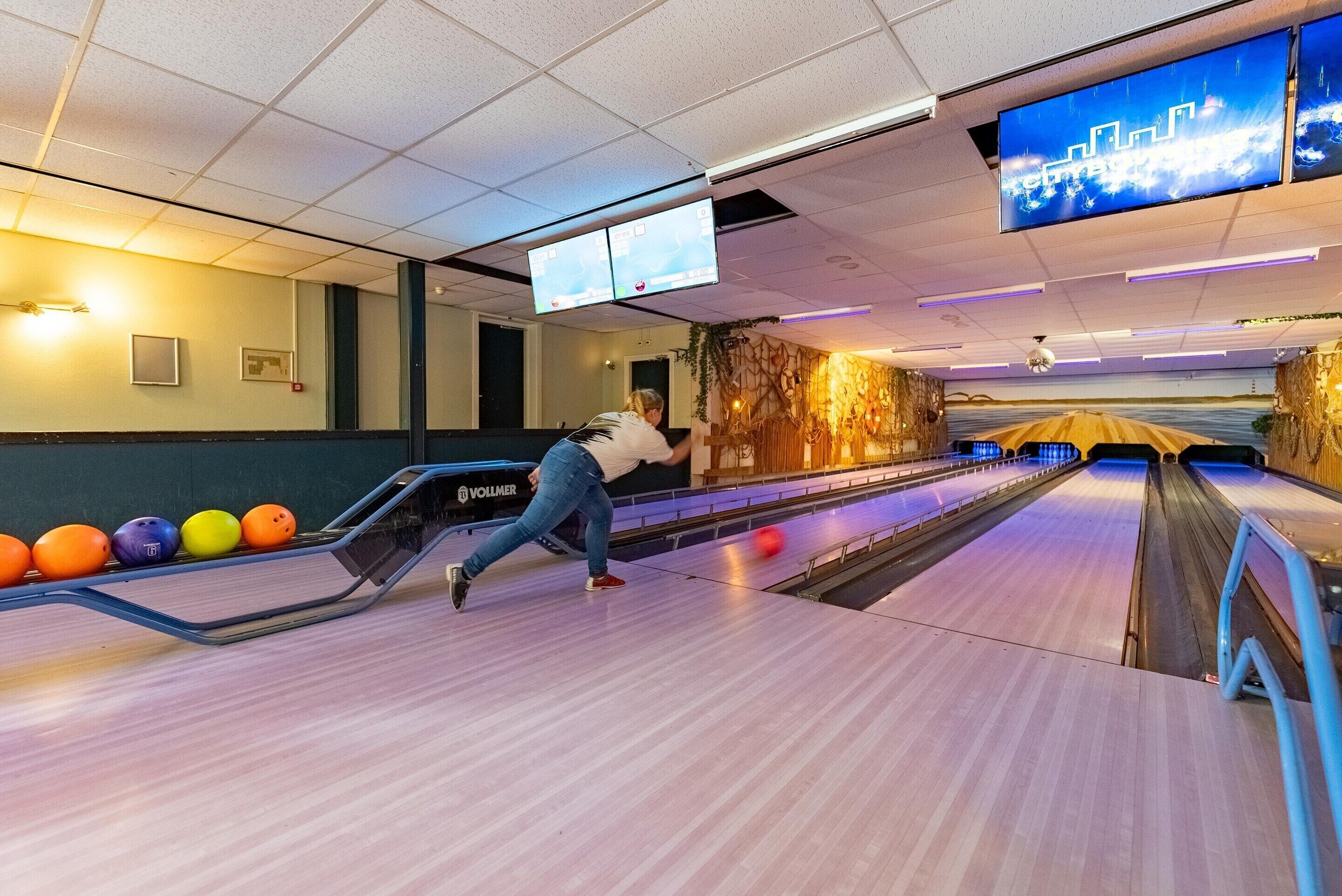 A bowling alley with multiple lanes, a person bowling, and overhead digital scoreboards.