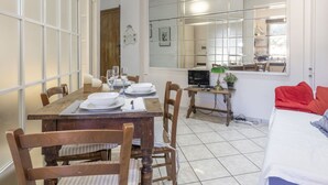 A dining area with a wooden table set for four, a kitchen visible through a large mirror, and a bed with red and grey bedding in the foreground. - Cosy apartment for 4 people with WIFI, TV, balcony and pets allowed (Sanremo)