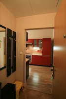 Un pasillo estrecho que conduce a una cocina con armarios rojos y un refrigerador de acero inoxidable.