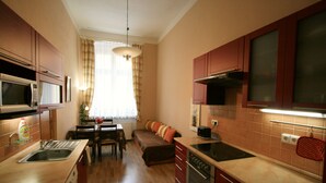 A compact kitchen with a microwave, stove, and oven. There is a dining table with chairs and a sofa in the center. - Apartment No. 19 Jaltská 3 (Karlovy Vary)