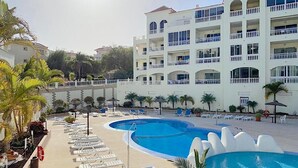 Ein Resort mit großem Poolbereich, zahlreichen Liegestühlen und einem mehrstöckigen Gebäude mit Balkonen.
