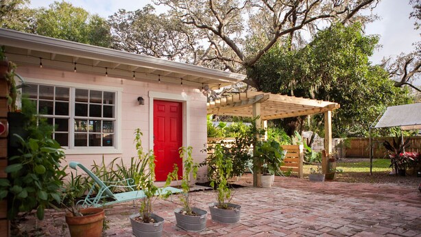 Una casa con puerta roja, patio de ladrillo y plantas en macetas.