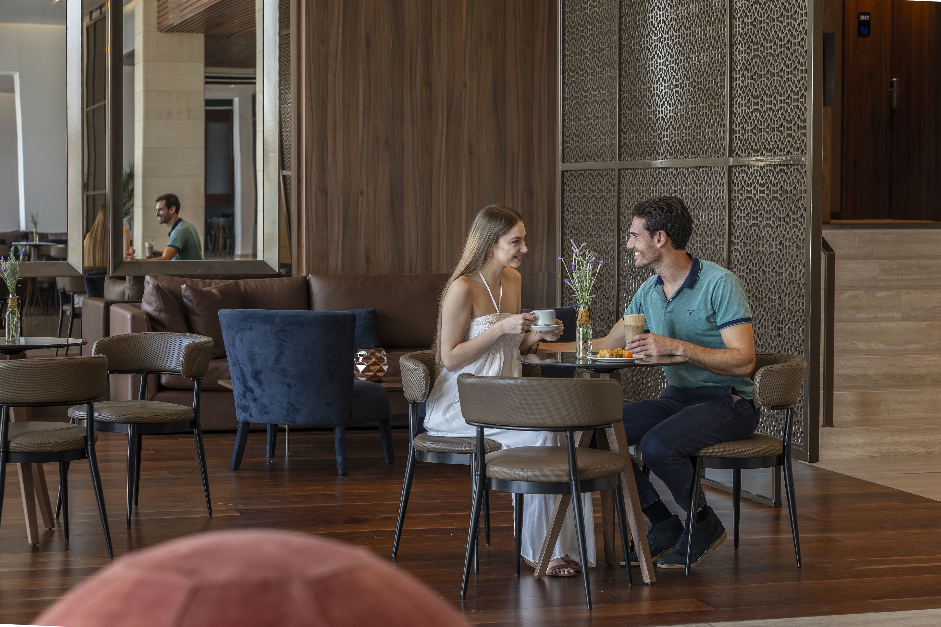 A modern indoor dining area with wooden flooring, cushioned seating, and a decorative wall.
