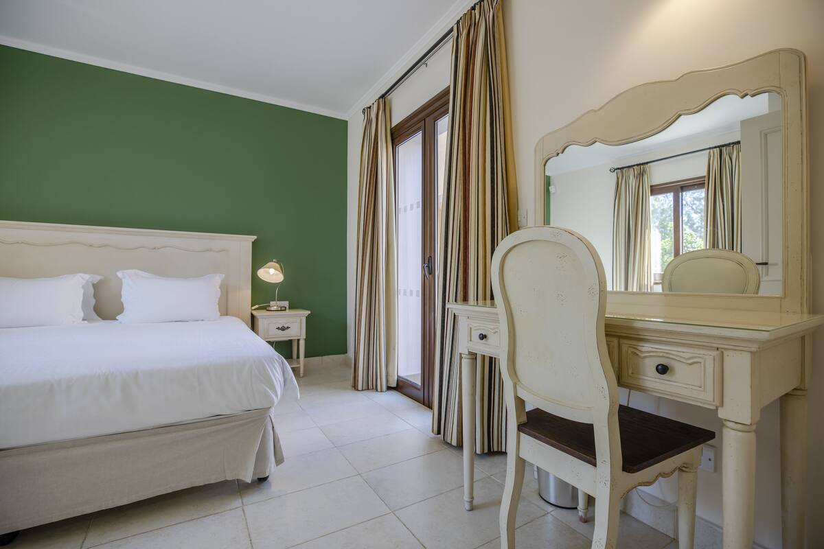Une chambre à coucher avec un lit, un bureau, une chaise, un miroir et des rideaux.