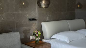 Una habitación de hotel moderna con pared de mármol, una mesita de noche con un jarrón de flores, una cama con ropa de cama blanca e iluminación de techo con textura.
