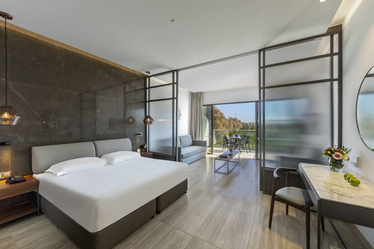 Une chambre d’hôtel moderne dotée d’un grand lit, d’un bureau et d’un balcon avec vue.