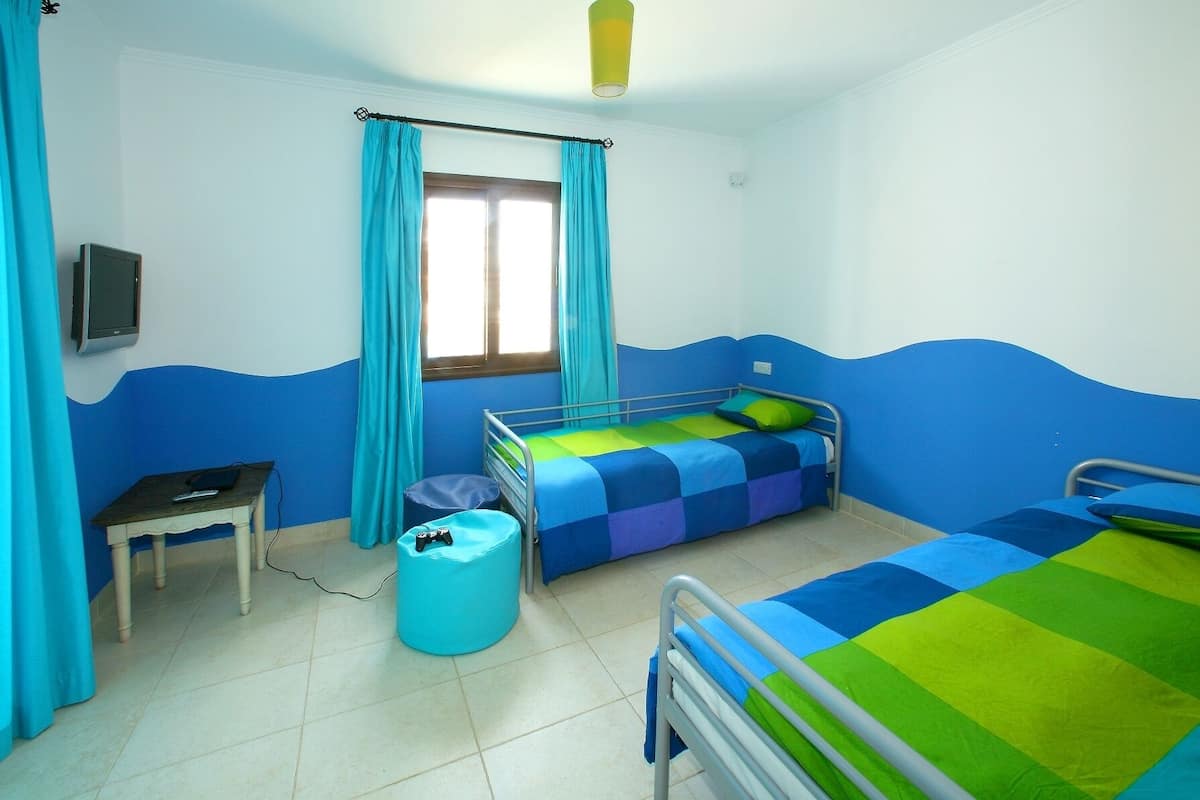 Une chambre avec deux lits, une petite table, une chaise, un téléviseur et une fenêtre avec des rideaux.